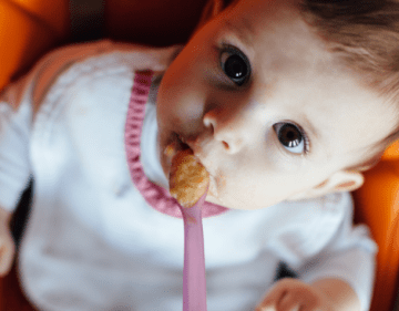 Infant looking up while eating spoonful of food