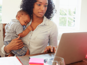 Woman holding infant while looking at laptop 