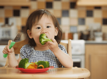 Toddler in high chair eating broccoli and carrots